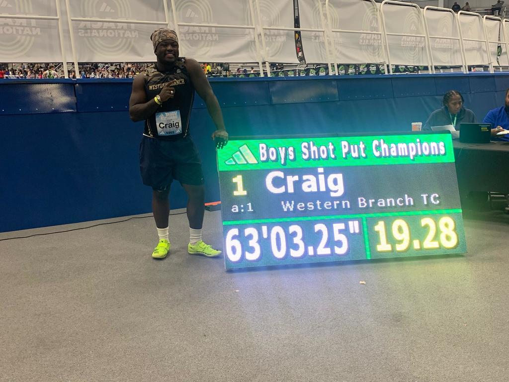 Student standing proudly by shot put results sign (first place)