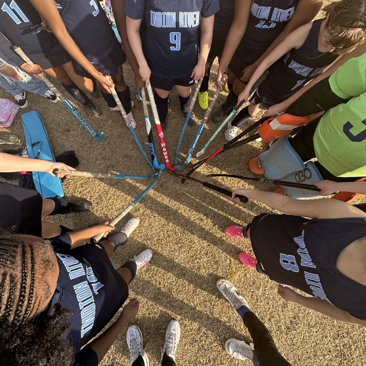 girls field hockey team in a huddle with sticks together