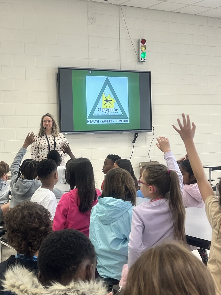 Several third-grade students sit facing a presenter, with multiple students raising their hands to participate during a Chesapeake Mosquito Control presentation displayed on a screen at the front of the room.