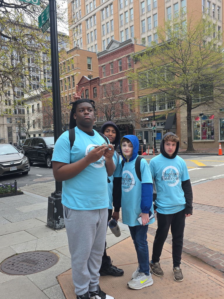 A group of 8th grade students smiling and posing together on the street