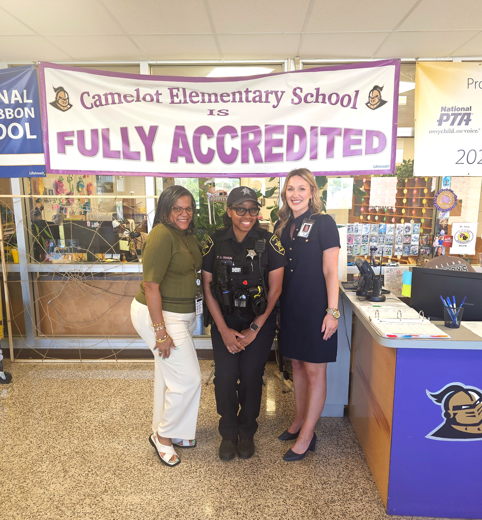 3 ladies standing together in front of Camelot elementary school's fully accredited banner