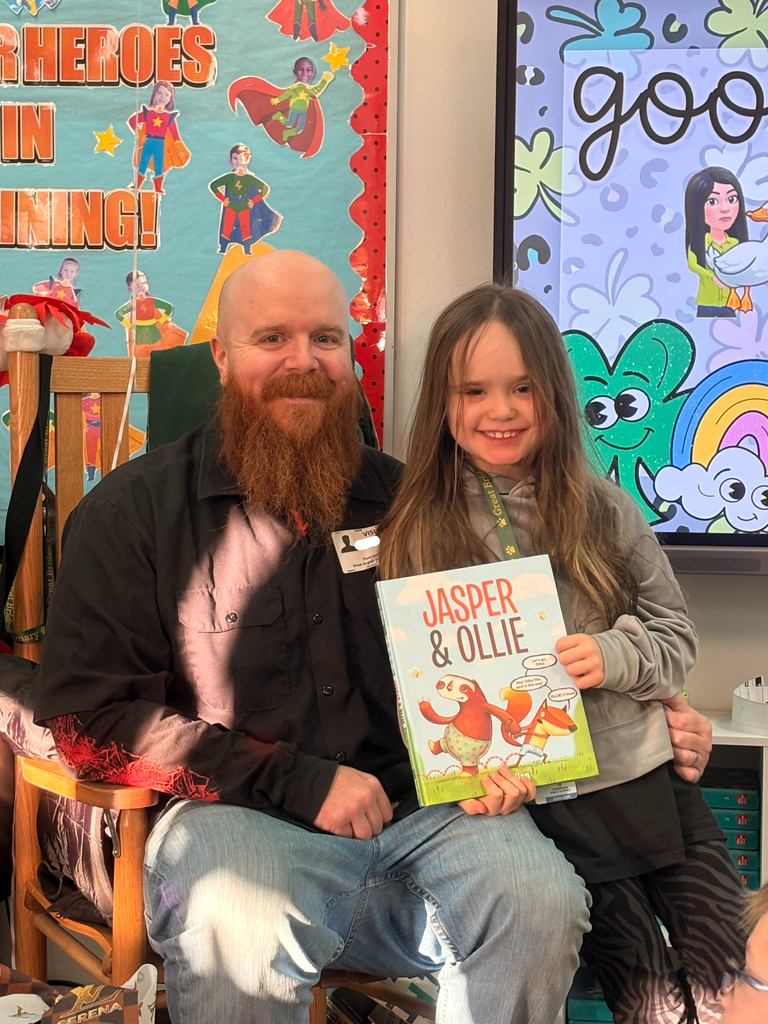 A student smiles beside their parent, who volunteered as a guest reader in Ms. Shinn’s classroom.