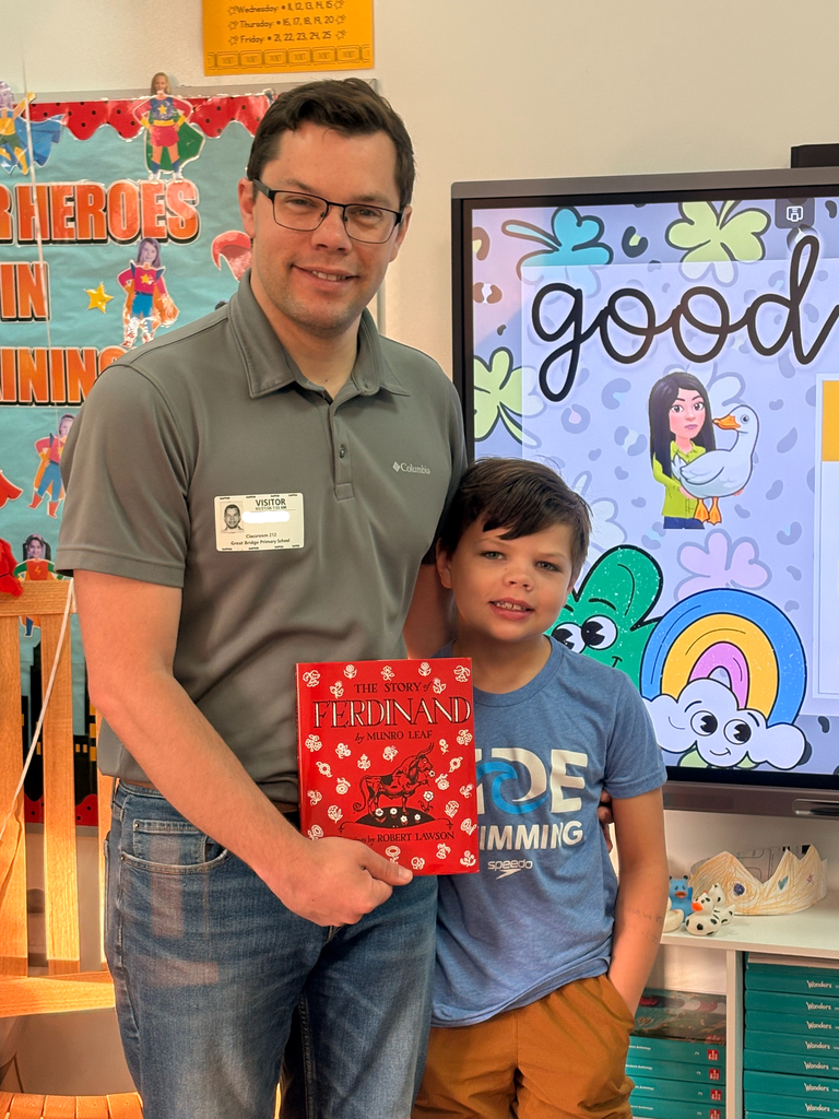 A student and their parent, a guest reader, pose together in a 2nd grade classroom setting.
