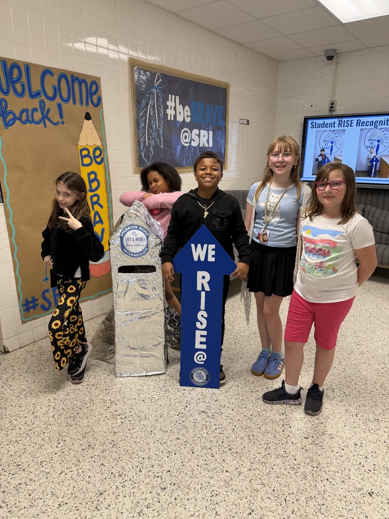 Students proudly standing by the RISE and Review rocket with the We RISE arrow.