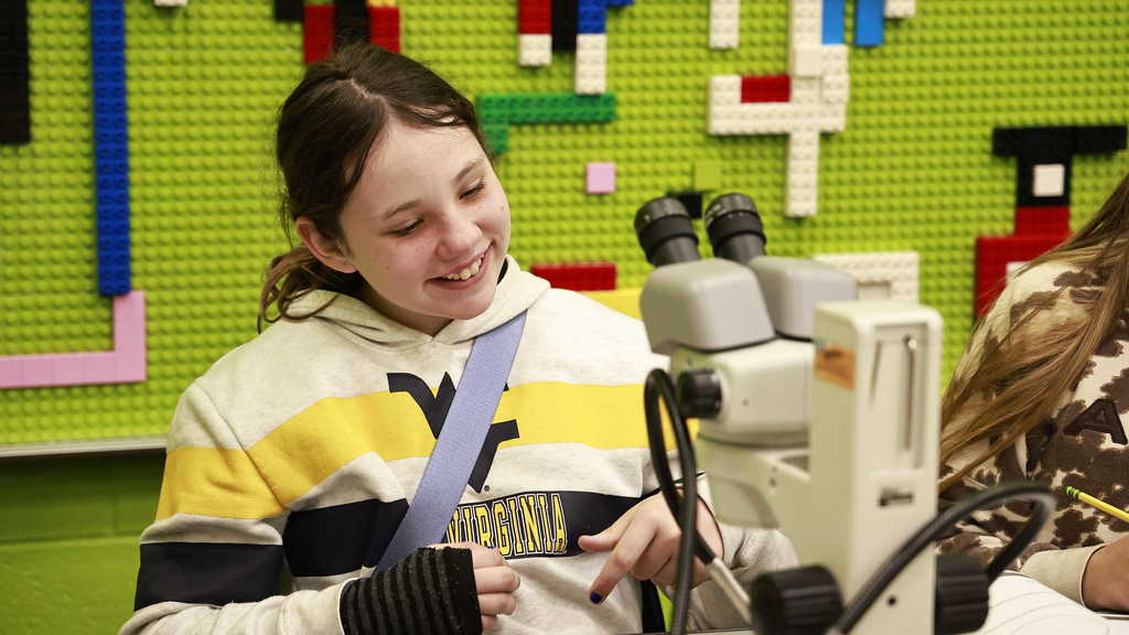 A student smiles as she gets ready to view a sample in a microscope