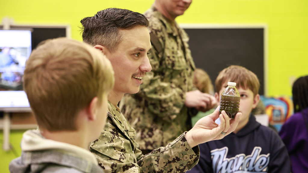 A member of the navy demonstrates a science lesson to students