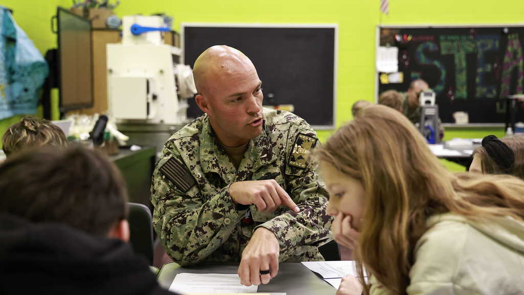 A member of the navy demonstrates a science lesson to students