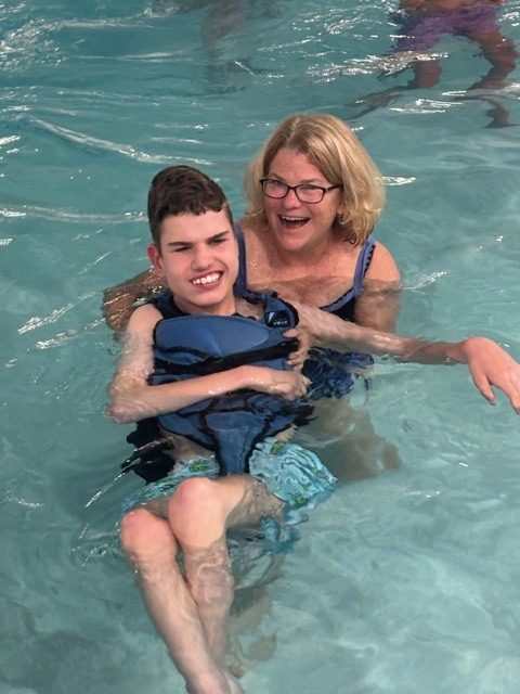 Teacher happily holding a student in the pool, both smiling and enjoying the day at the YMCA