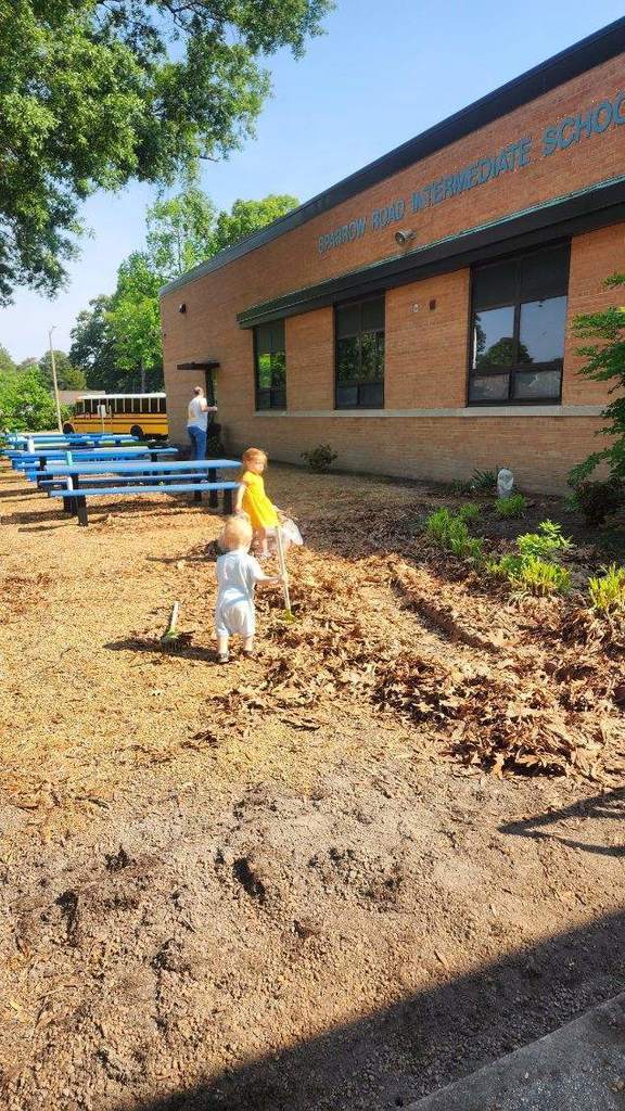Two little kids helping clean up outside the school.