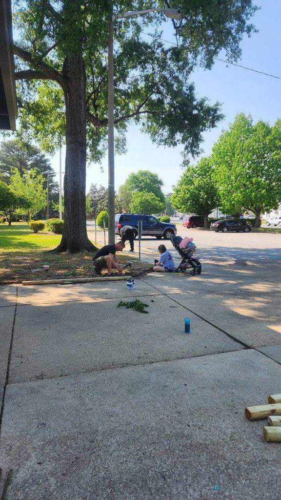 Family cleaning up the bed around a tree and sidewalk.
