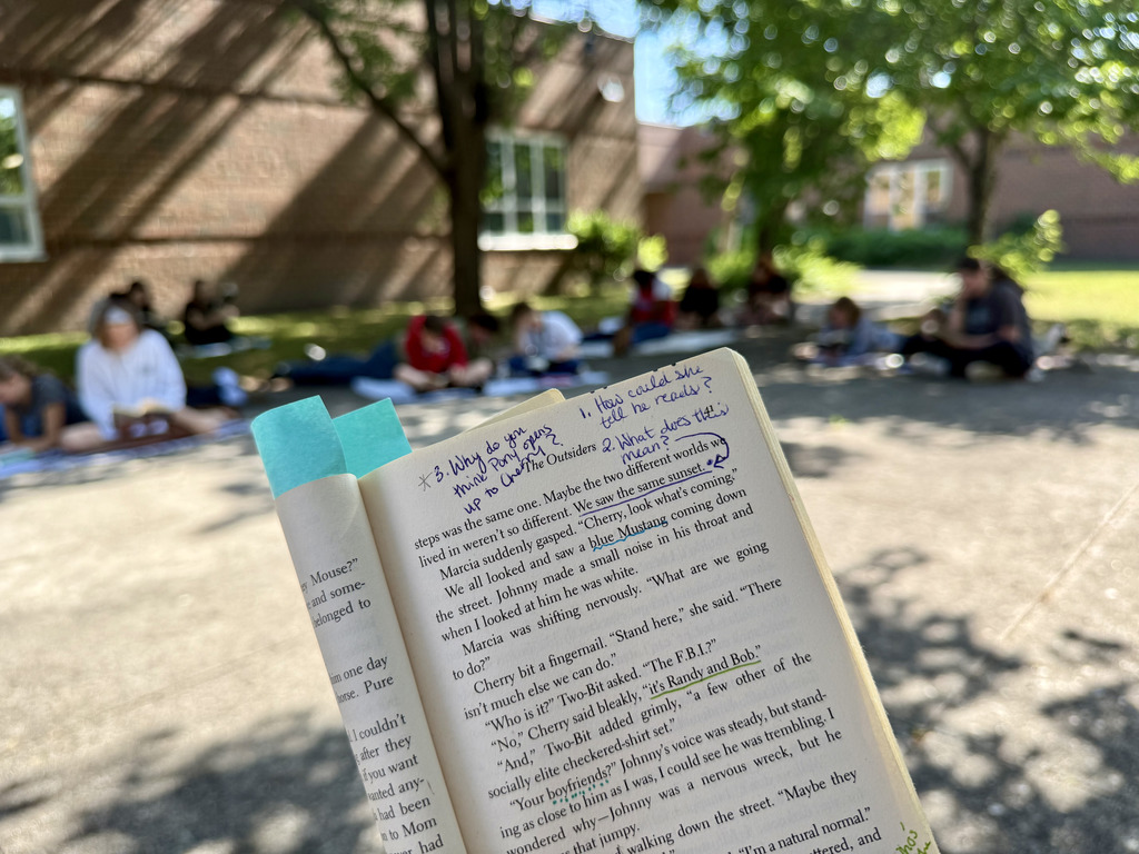 annotated book in front while students work in the background while reading outside