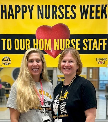 Two female staff members smile in front of a high-contrast yellow and black banner that reads "Happy Nurses Week, Thank You, HOM Nurse Staff.