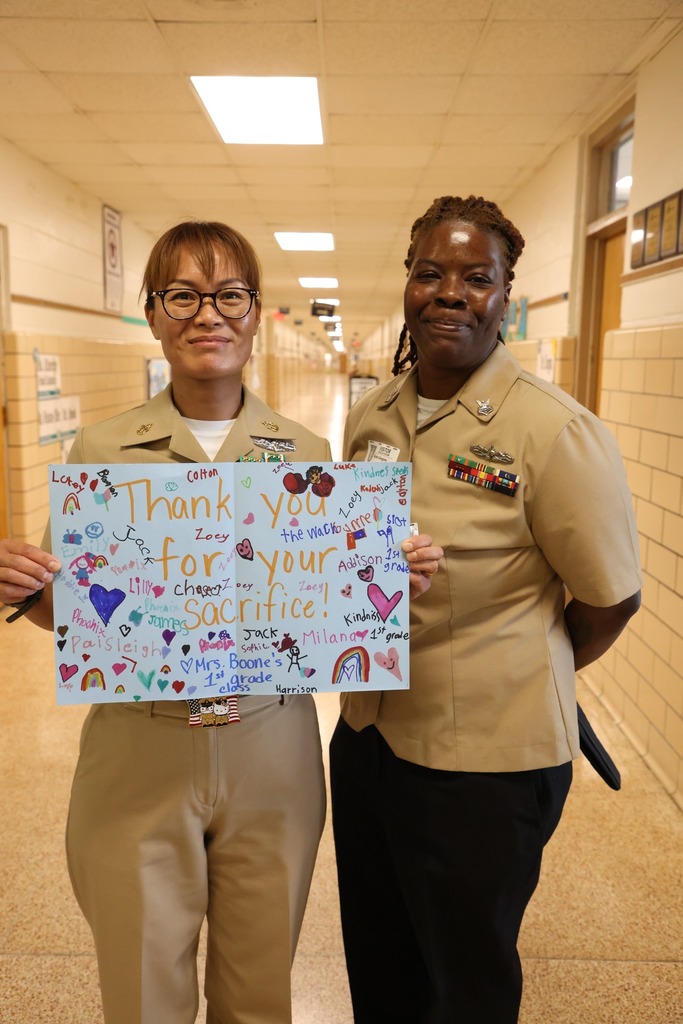 Military team members for NSA proudly hold up Thank you card from students