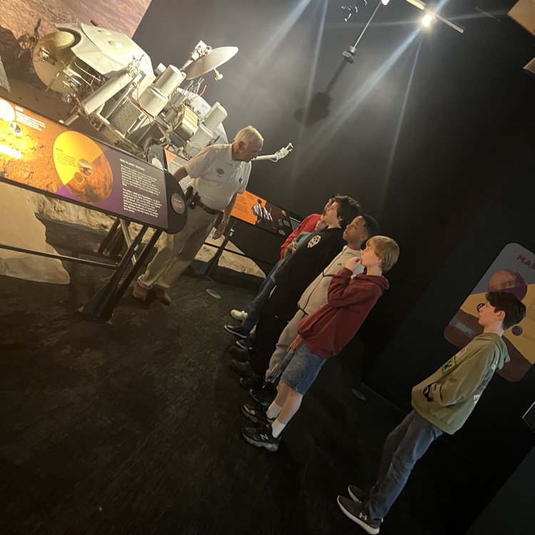 students in front of volunteer discussing spacecraft.