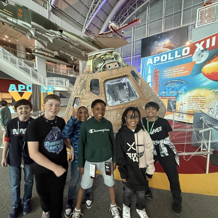 students smiling in front of space exhibit. 