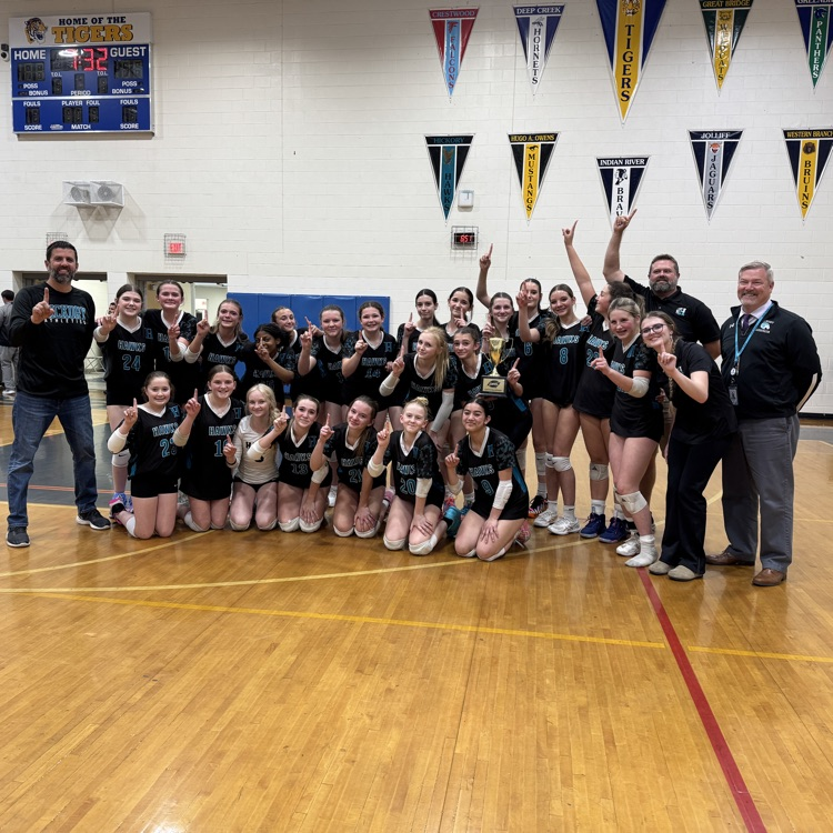 girls volleyball team, coaches, and principal proudly display a number one finger and the championship trophy