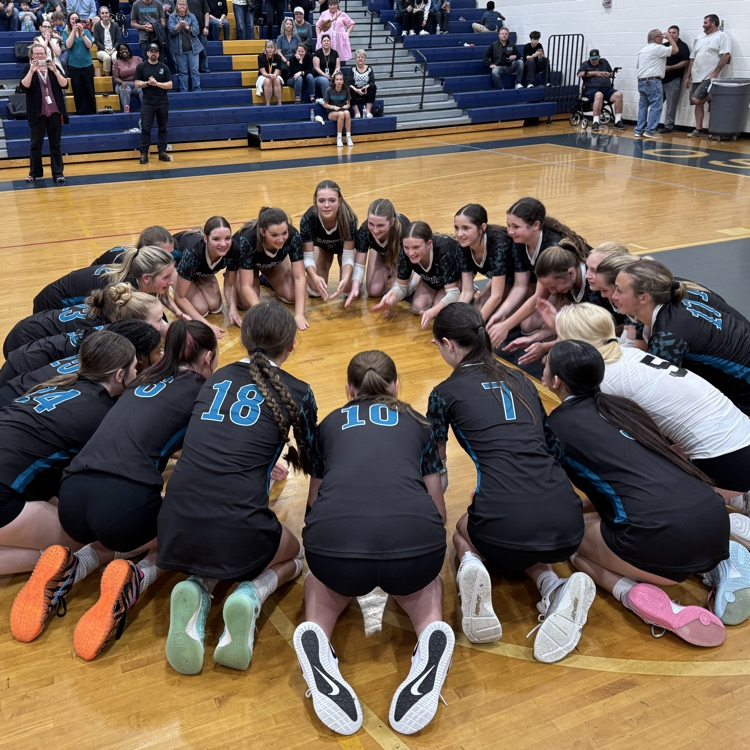 girls volleyball team huddled on court for their final cheer