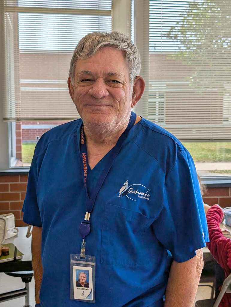 A staff member wearing a blue scrub-style shirt with a Chesapeake Public Schools logo.and a visible  badge.