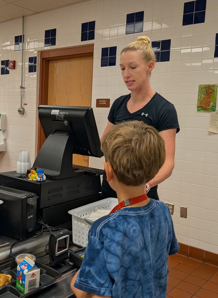 A cafeteria staff member sitting at a computer terminal at the end of the lunch line, checking out a student. 