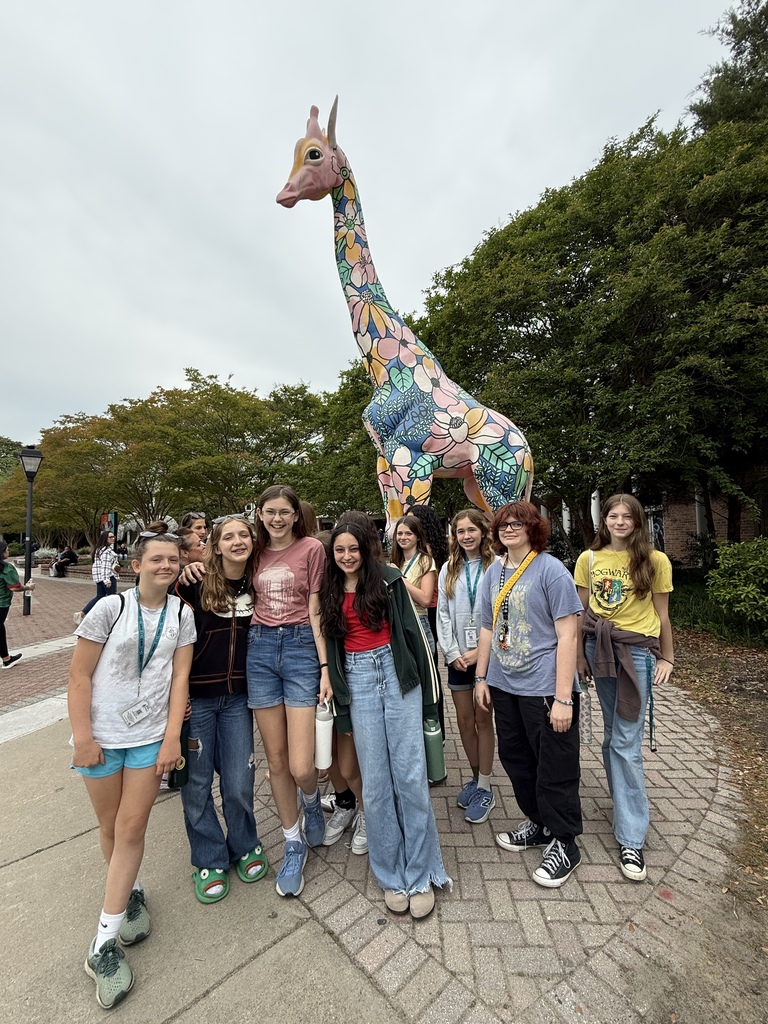 a group of students smiling in front of a giraffe statue at the zoo