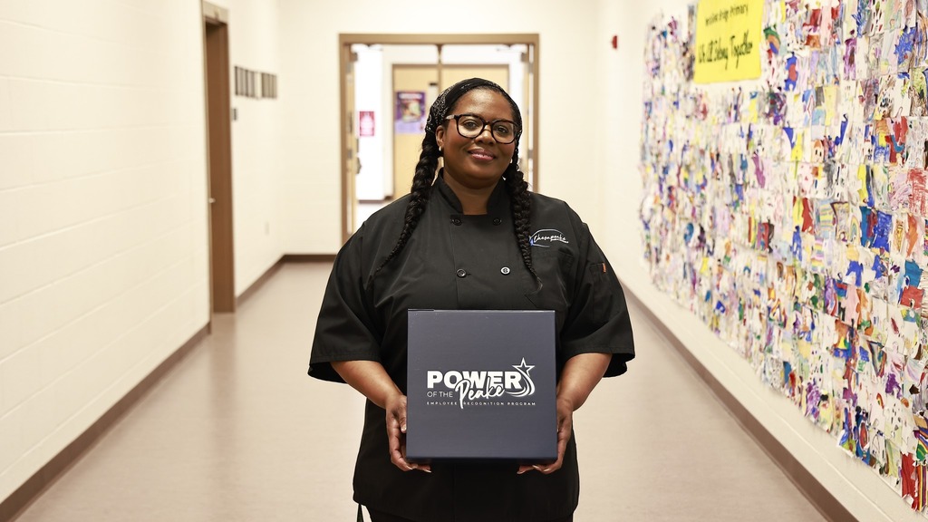 Mrs. Moore, cafeteria manager, smiling while holding her “Power of the Peake” award certificate in recognition of her outstanding support of students and staff.