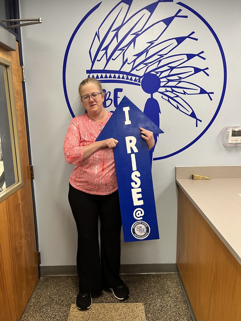 Staff member standing in the main office proudly holding the I RISE sign.