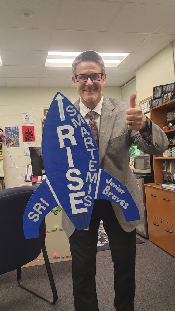 Mr. Triolet smiling proudly with new I RISE rocket sign "Smartemis".