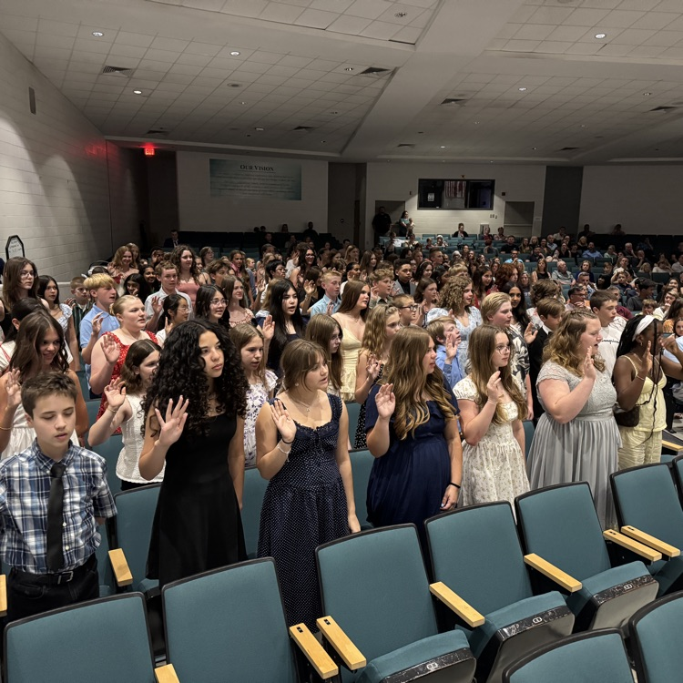 students standing in the auditorium reciting the pledge