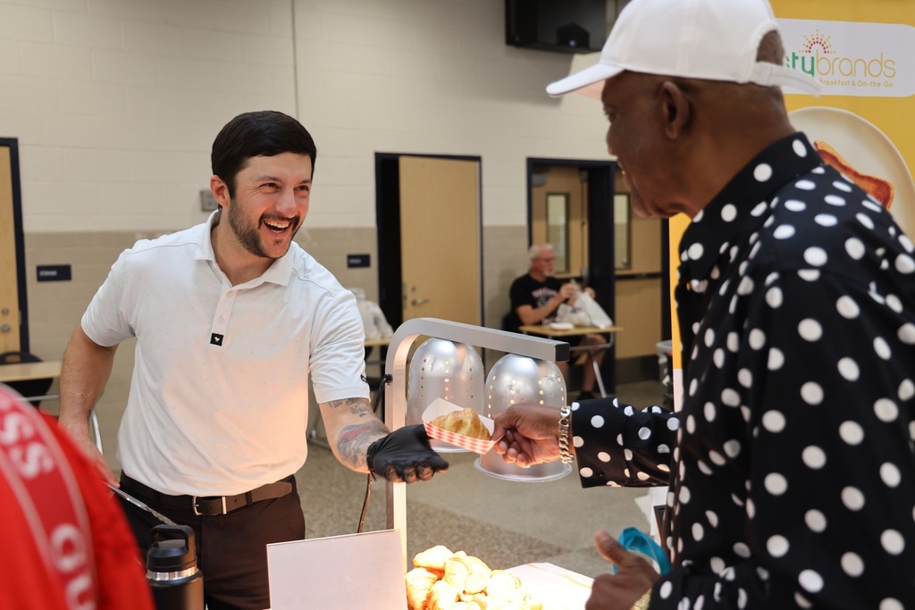 A food vendor handing a sample croissant to a community member.