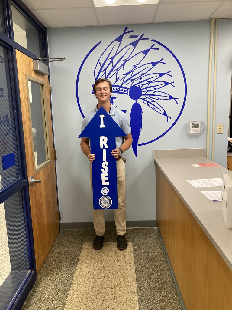 Staff RISE award winner smiling and holding the RISE arrow.