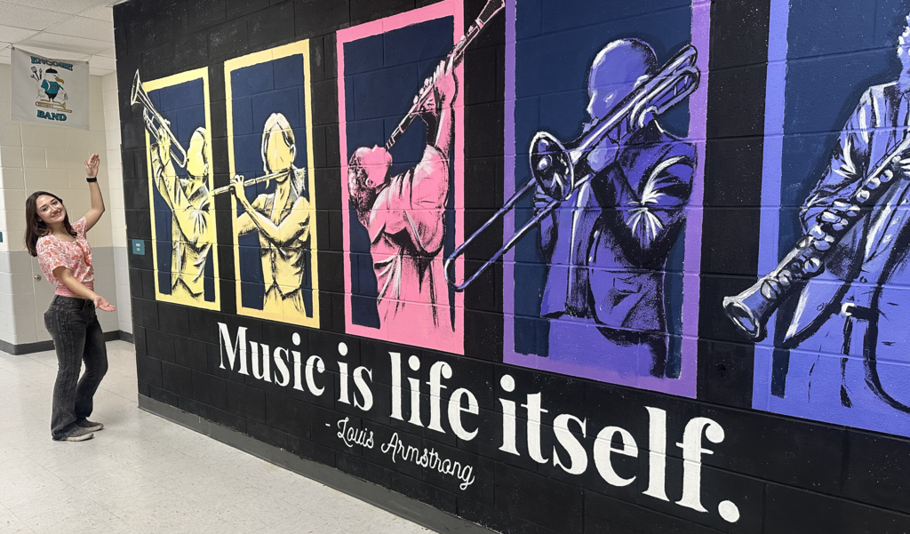 Student standing proudly with mural