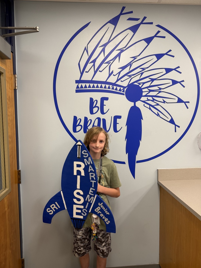 Smiling student proudly holding up the I RISE rocket-Smartemis for turning in the Math Review IXL skills sheet.