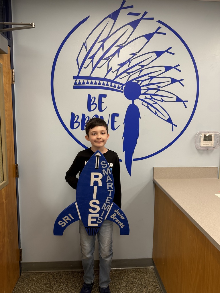 Smiling student proudly holding up the I RISE rocket-Smartemis for turning in the Math Review IXL skills sheet.