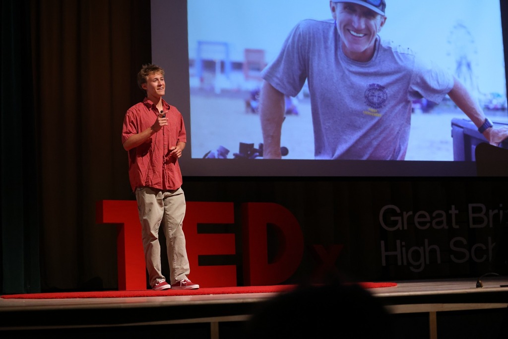 Student speaking on stage with a projector in the background.