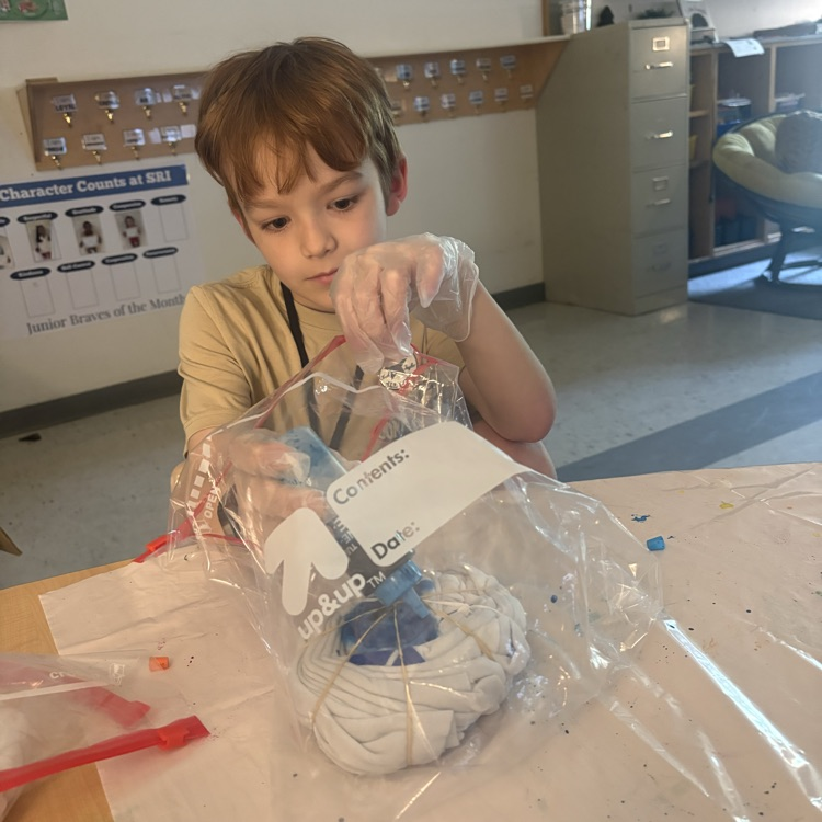 Student focused on tie dying their own shirt using rubber bands and a bag with different colors.