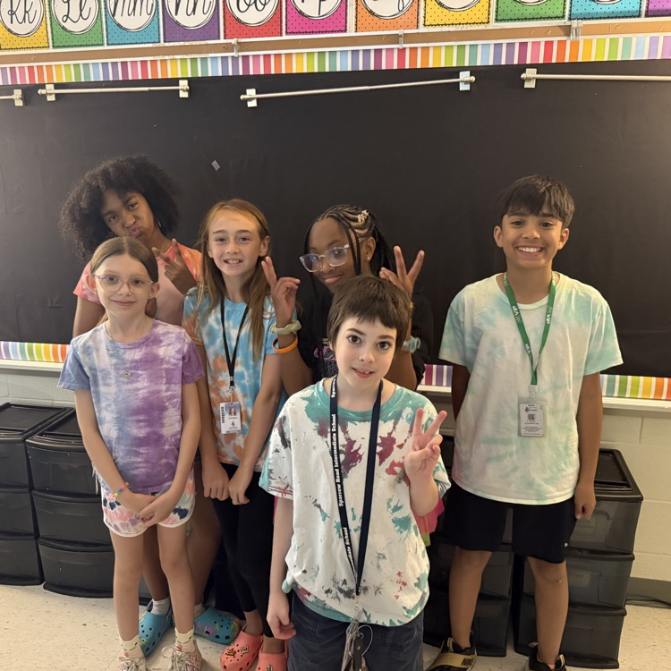 A group of elementary students smiling together in the classroom, wearing vibrant tie-dye shirts to celebrate Student Appreciation Week.