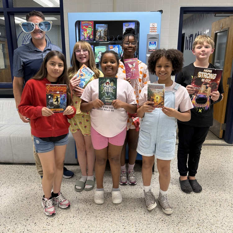 A group of smiling students holing up their selected book with Mr. Triolet.