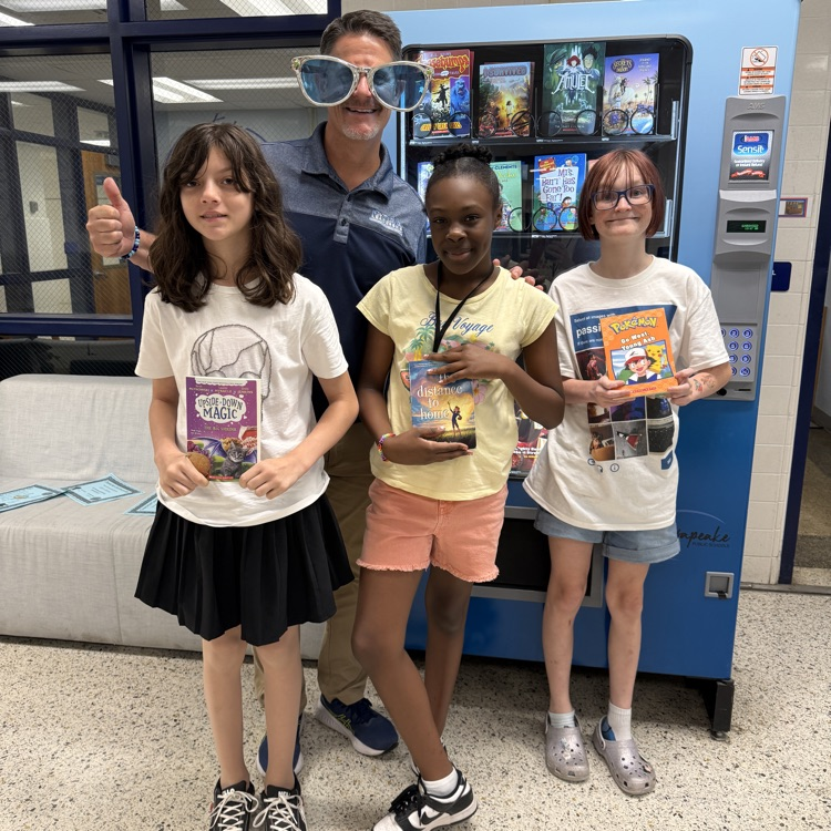 A group of smiling students holing up their selected book with Mr. Triolet.