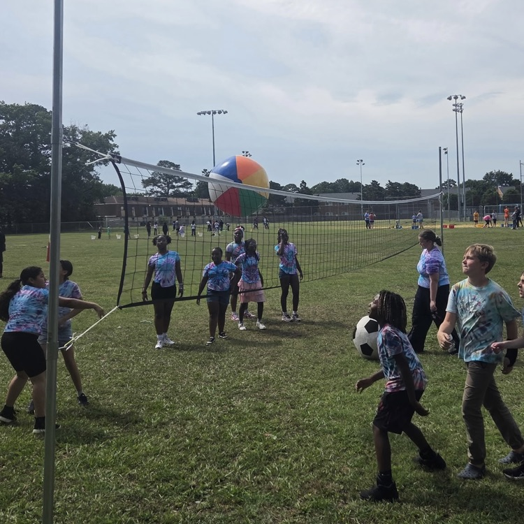 Students wearing tie dye shirts outside playing volleyball. 