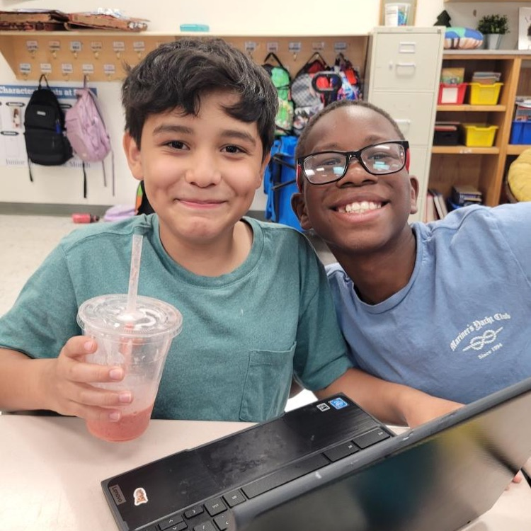 close up of two smiling students with a chromebook and smoothie. 