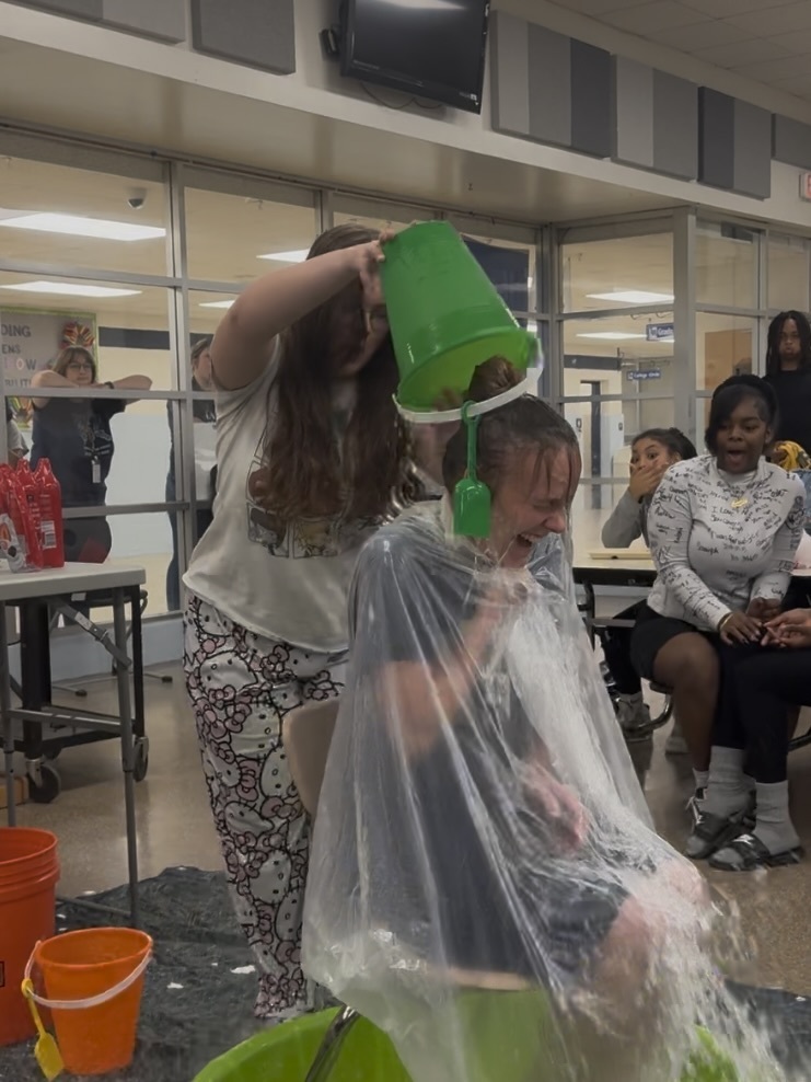 Students dump a bucket of cold water on a teacher during a Field Day activity.