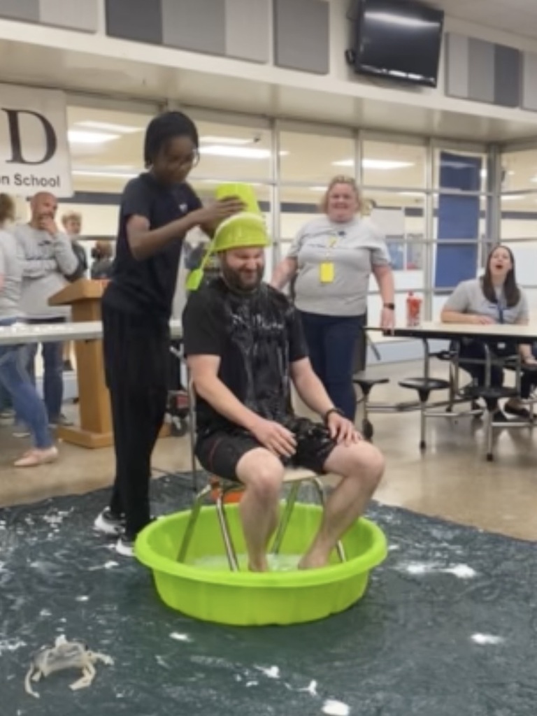 Students dump a bucket of cold water on a teacher during a Field Day activity.
