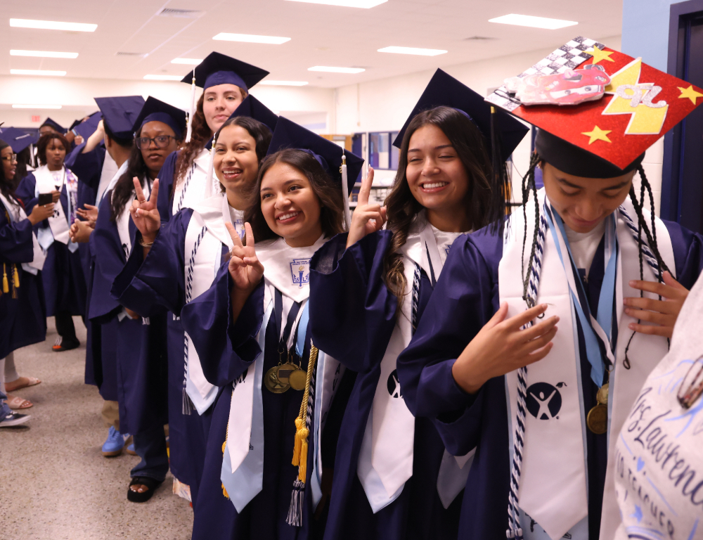 IRHS students in the cafeteria lining up and smiling with their caps and gowns.