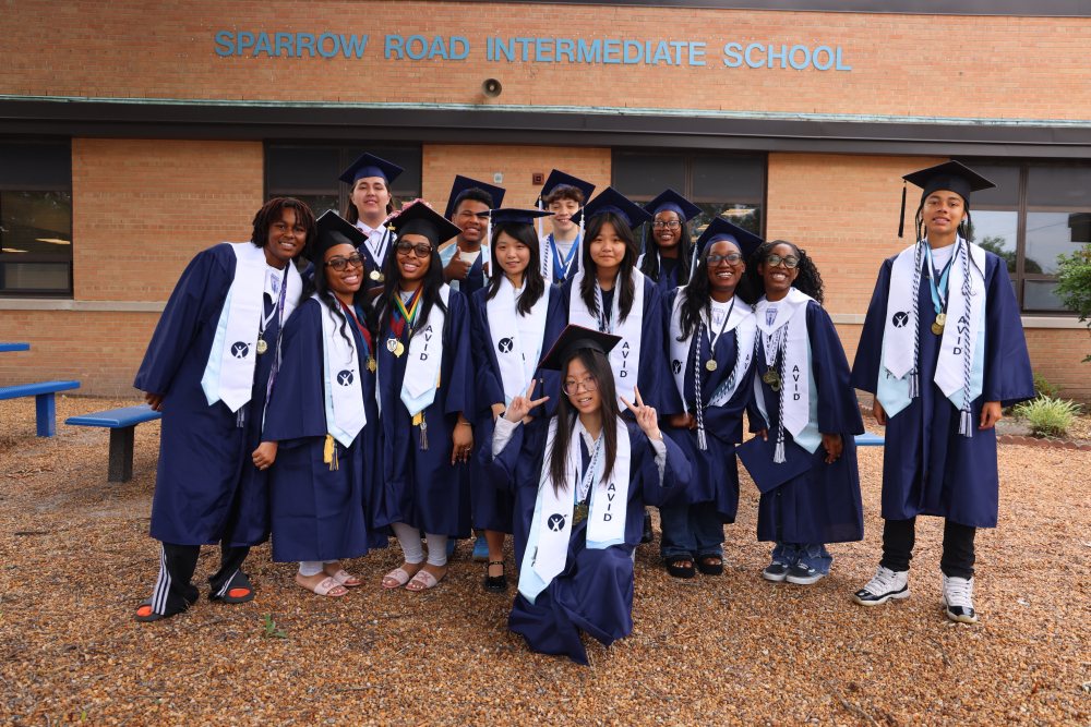 Group of IRH students smiling in their caps and gowns in front of SRI.