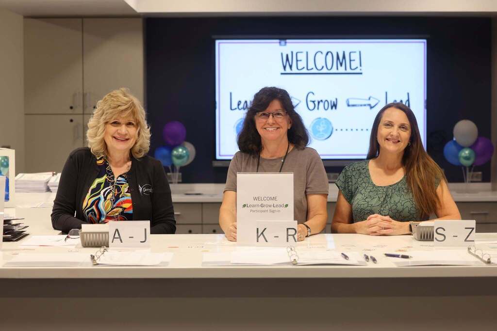 The check in area at the conference with three employees smiling welcoming people in.