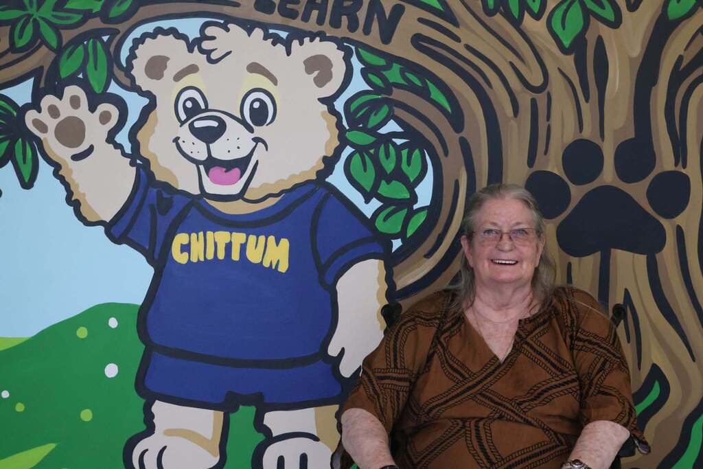 Ms. Chittum happily smiles with Chittum Bear Mural