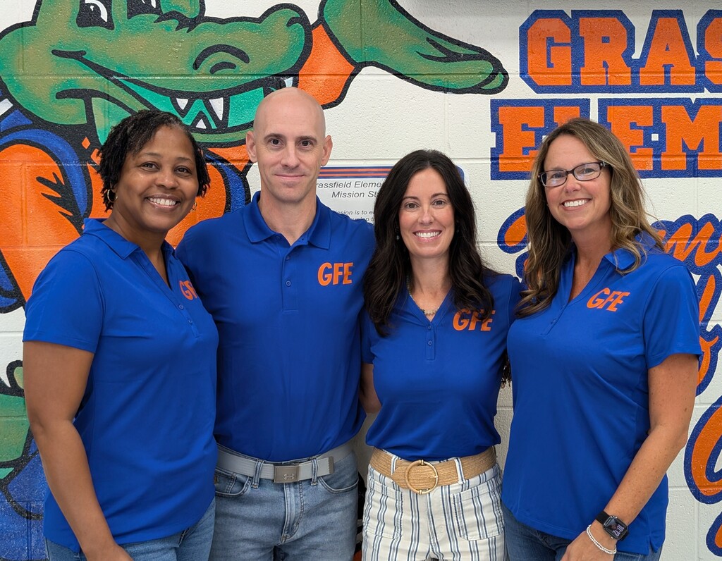 Photo of the GFE Administration standing in front of a wall that is decorated with bright orange and blue Grassfield Elementary colors. The display features Gator-themed decorations and school spirit elements, creating a welcoming back-to-school atmosphere.