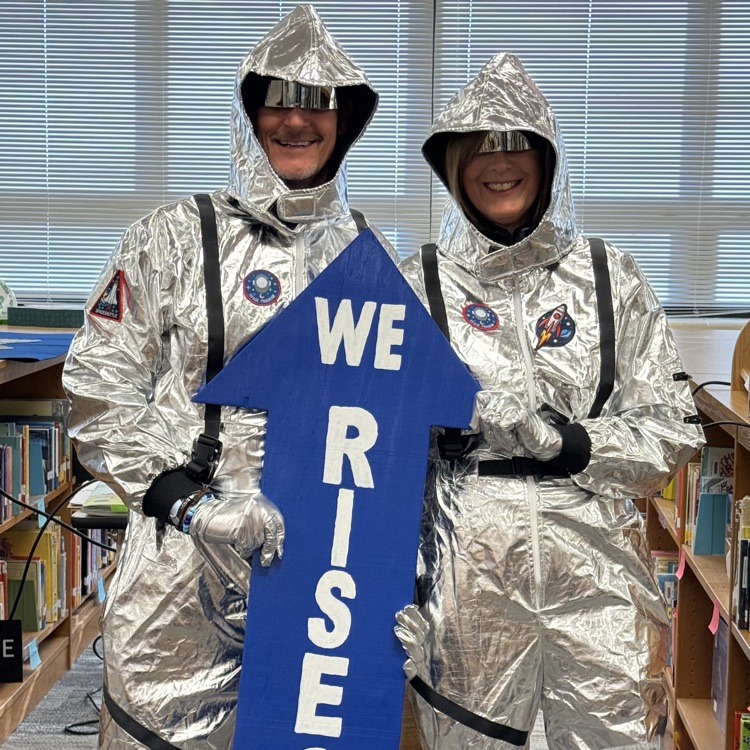 Mr. Triolet and Mrs. Boerboom in space suits holding up a We RISE at SRI sign.