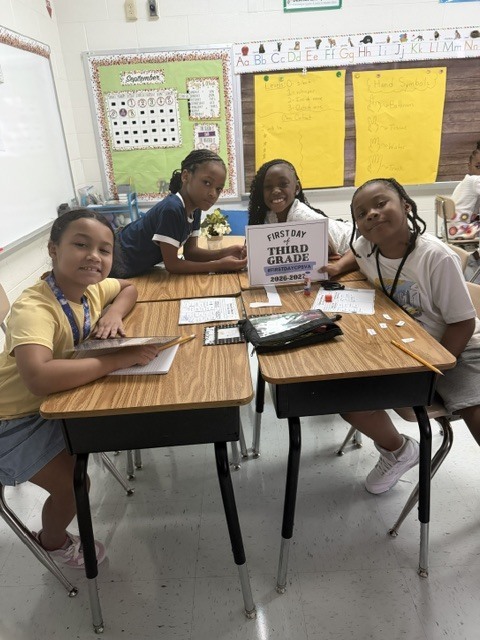 third graders pose with first day of school sign