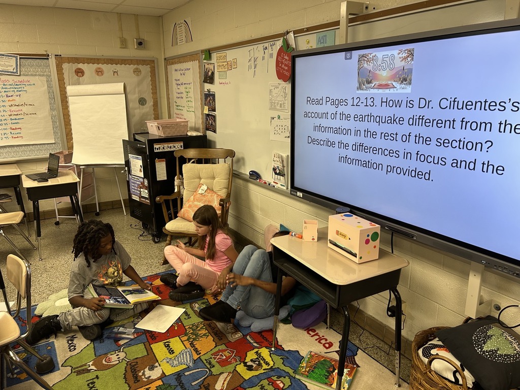 Students working on the classroom floor, using textbooks and whiteboards to answer reading questions together.